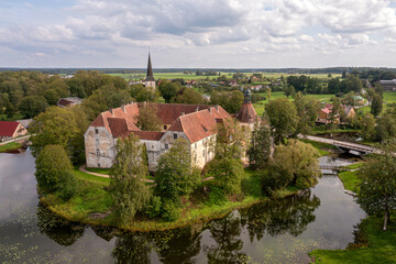 Fototapeta premium Aerial View of a Stone Castle Surrounded by Water and Trees in Rural Latvia