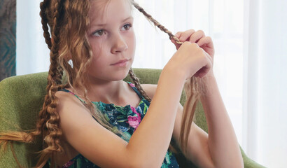 Teenage girl unbraiding pigtails in room on chair. Beauty and hair care. 