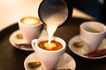 Stainless steel milk pitcher pouring into a coffee cup to make a cappuccino