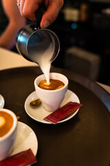 Waiter's hand pouring milk with the pitcher into a coffee cup. Vertical
