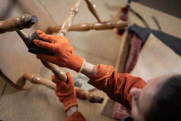 Restoration of wooden chair. Young carpenter sanding chair legs with sandpaper, female restorer in a workshop