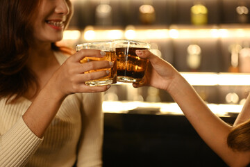 Close up shot of two friends toasting with drinks in the bar. Nightlife, celebrations and friendship concept