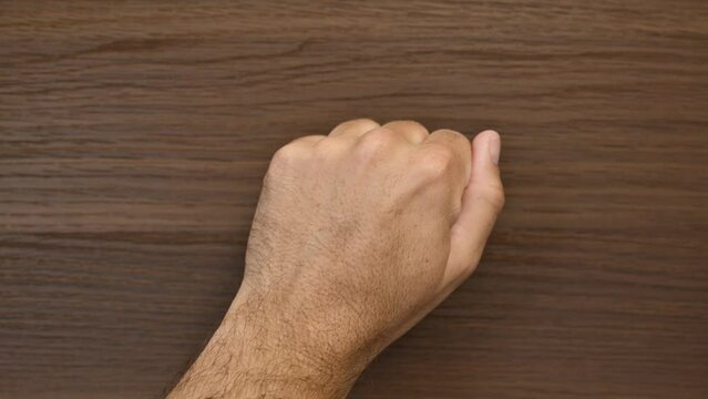 A close-up image of a person's hand knocking on a wooden door, symbolizing the act of seeking entrance or attention, with the hand forming a closed fist against the textured wood surface.