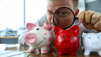 Man examining tree funny piggybanks with magnifying glass portrait