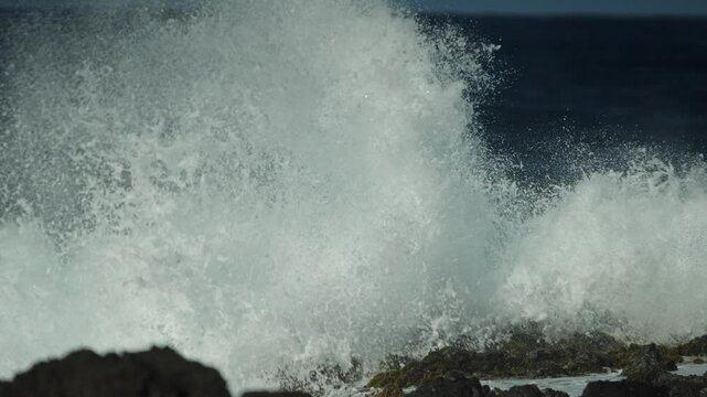 Strong waves of water hitting the rocks at the seashore and splashes up high, closeup 