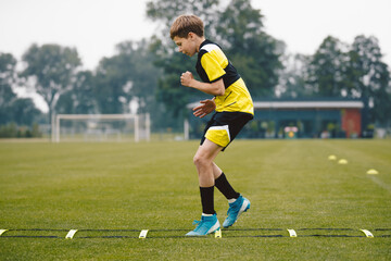 Youth soccer player skipping on training ladder. Young boy running fast and exercising using training equipment. Football player improving speed on training pitch