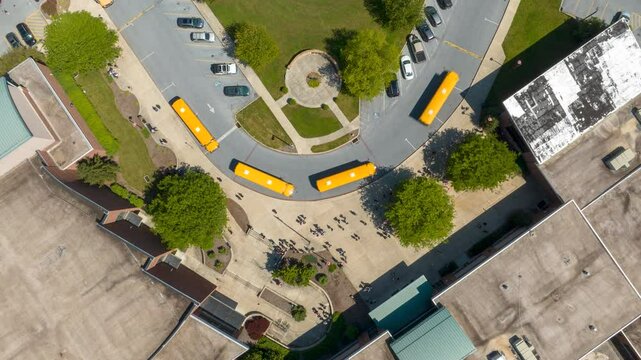 American school dismissal time lapse above bus loop. Aerial hyperlapse of students walking out of public high school building and entering yellow buses to go home.
