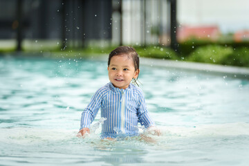 happy toddler baby playing water splashing in swimming pool