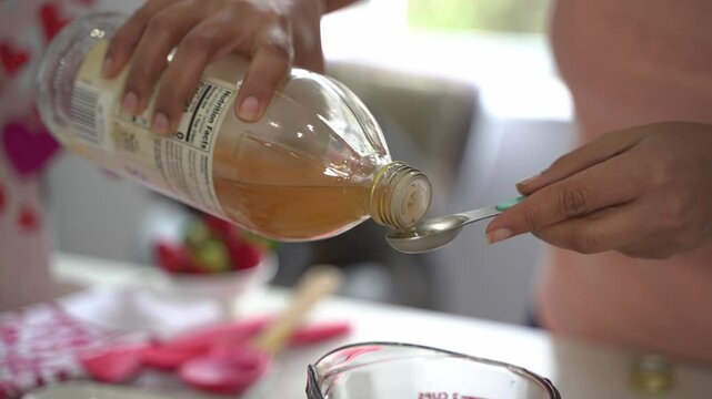 Pouring a teaspoon of apple cider vinegar making a special valentine's day cake vegan chocolate cake eggless plant based dairy free