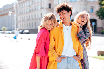 Group of young three stylish friends posing in the street. Fashion man and two cute female dressed in casual summer clothes. Smiling models having fun. Cheerful women and guy outdoors