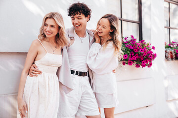 Naklejka premium Young three stylish friends posing in the street. Fashion man and two cute female dressed in summer clothes. Smiling models having fun. Cheerful women and guy outdoors, in sunny day, Europe, Santorini