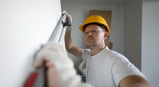 Male inspector in protective gloves hold building level in hand portrait. Checks the quality of constructed walls. Bilding inpections concept.