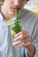 Fototapeta premium Young man wearing light blue shirt drinking mojito cocktail drink with drinking straw