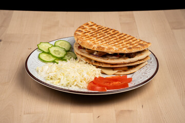 Plate of grilled pita sandwiches with shredded cabbage, cucumber slices, and tomato slices on wood