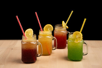 Colorful drinks in mason jars with straws and lemon slices on wooden table against black background