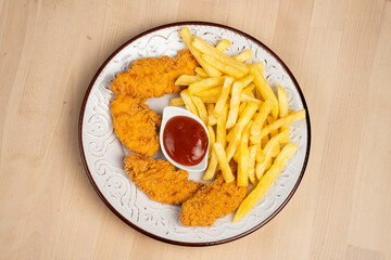 Plate of crispy fried chicken wings with French fries and a side of ketchup on a wooden table