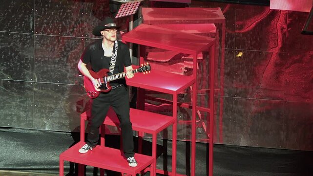 Man in cowboy hat plays red electric guitar on stage, copy space