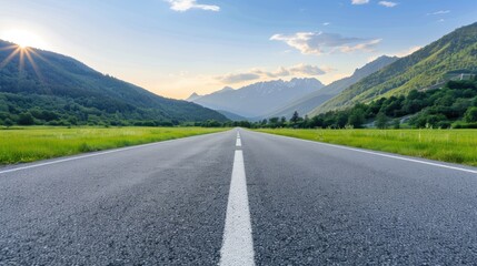 Naklejka premium A long, empty asphalt road with a white dividing line leads towards a mountain pass, surrounded by lush green trees and majestic snow-capped peaks under a clear blue sky