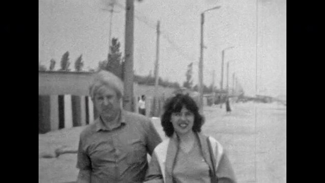 Happy adult married couple walking in summer outdoors. Smiling woman, man lovers walking holding hands at beach resort. Mature love. Vintage Black white film. Family retro 1970s archive lifestyle