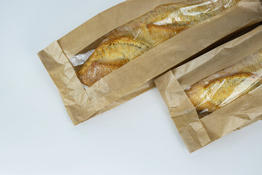 Closeup of two french baguettes in the brown kraft paper plastic bag isolated on white background. Fresh baked bread for sell. High resolution studio photo. Minimalist design. Top view. Copy space.