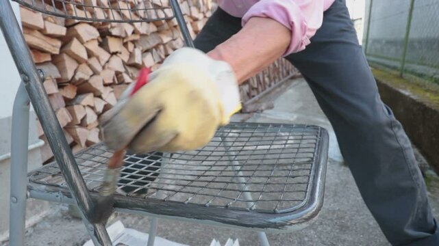 Man using brush to paint an object. Worker in backyard painting a chair
