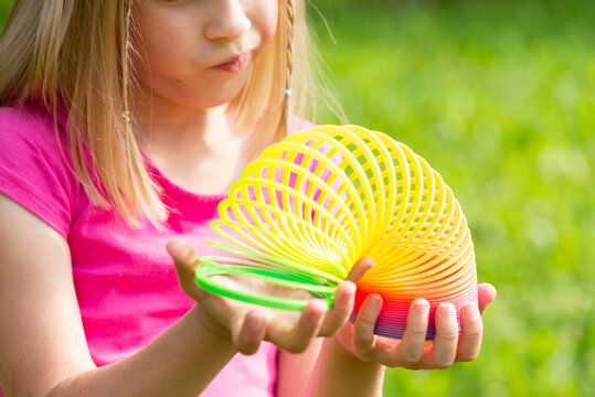 Blonde girl plays with a rainbow spiral children's toy. 90s toy, nostalgia, retro.