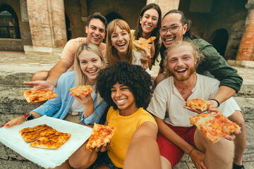 Multicultural smiling friends eating pizza sitting outside - Cheerful young people taking selfie photo with smartphone outdoor - Happy life style concept with guys and girls hanging out on a sunny day