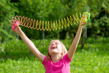 Happy girl with stretched rainbow spiral children's toy in the hands on a background of green...