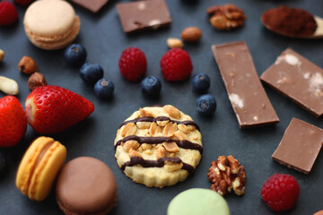 Macarons, chocolate, cookies, berries and various nuts on dark blue background. Selective focus.