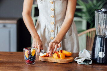 Close-up of a glass bowl with fruits and berries and a female hands.