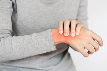 Close-up of a person in a grey top scratching their red, irritated wrist, indicating skin irritation or an allergic reaction.