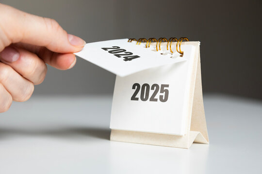 a woman's hand turns over a calendar sheet. year change from 2024 to 2025.