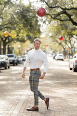 Fototapeta premium A blonde man in a white turtleneck and plaid pants poses on a street in Florida.