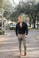 A handsome blonde man in a black shirt and plaid pants walks down a street in Orlando, Florida.