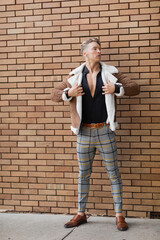 A handsome blonde man in stylish attire stands against a brick wall on the streets of Orlando, Florida.