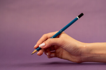 Beautiful female hand on an isolated on a purple background nude manicure hand with a blue pencil...