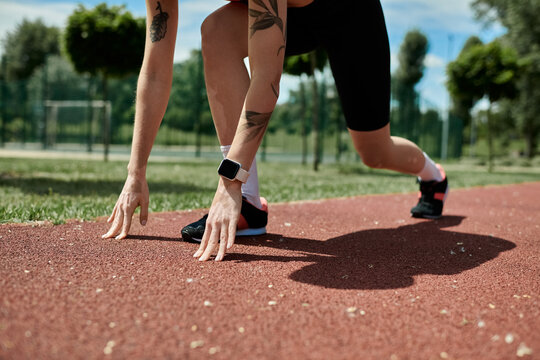 A young woman with vitiligo and a tattoo in active wear prepares to run on a track, her hand reaching for the ground.