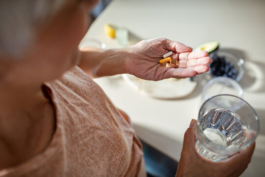 Senior woman taking daily vitamins and supplements with a glass of water