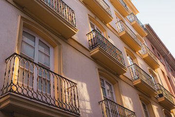 A facade of a building with multiple balconies in Valencia, bathed in warm sunlight. The repetitive patterns and shadows create a visually appealing urban scene.