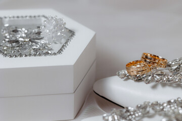 A white box with a pair of gold wedding rings inside. The rings are placed on top of a white shoe