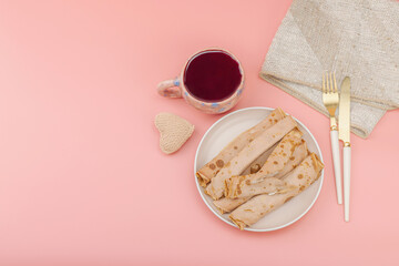 A cup of fragrant hibiscus tea and thin pancakes with cream. Good mood concept, cozy home comfort