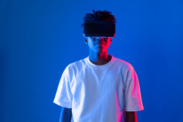 Surprised young African American looking through VR holding interesting object hologram on pink...