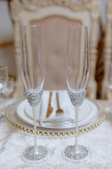 Two champagne flutes with gold beads on the stems are on a table. The table is set for a special occasion, and the glasses are placed next to each other