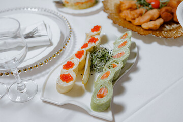 A white plate with sushi rolls and a green salad sits on a table. The sushi rolls are topped with red caviar and the salad has a green and yellow dressing. The table is set with silverware