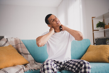 Photo of unhappy upset guy sleepwear pajama sitting home sofa having nech ache indoors house...