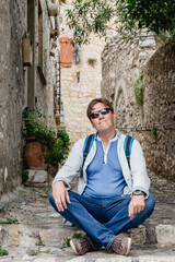 A traveler in sunglasses and a backpack relaxes in a peaceful alley with rustic architecture. Saint Paul de Vence. France. Provence.