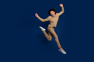 Fototapeta premium Full length photo of handsome young man running have fun dressed stylish beige garment isolated on dark blue color background