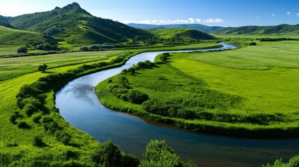 Naklejka premium A winding river flowing through a green valley with rolling hills.