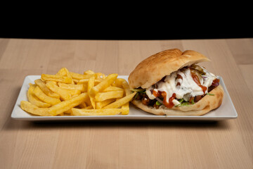 Delicious sandwich with fries served on a white plate over wooden table against a black background
