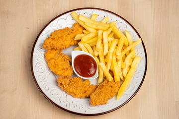 plate of crispy fried chicken wings with French fries and a side of ketchup on a wooden table
